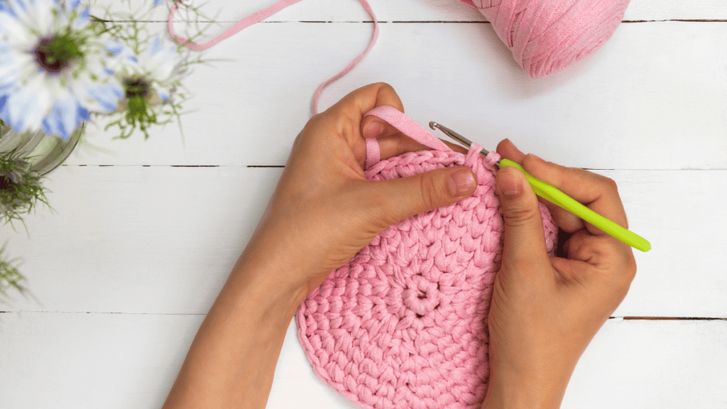 pink yarn with womans hands showing how to crochet a doll